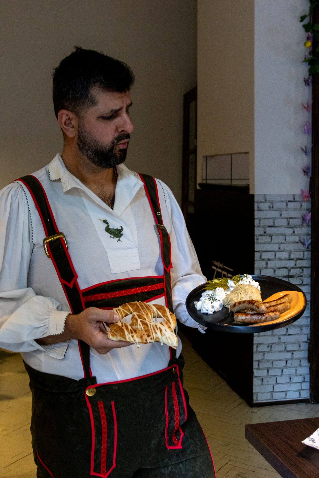 Bőrnadrágos felszolgáló perecet és kolbásztálat hoz